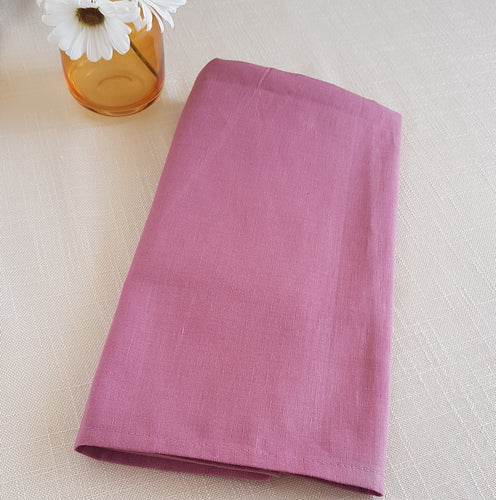 Folded pink fabric on a light beige surface with a small vase of flowers.
