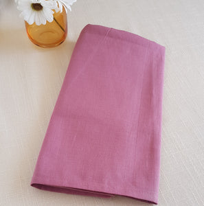 Folded pink fabric on a light beige surface with a small vase of flowers.