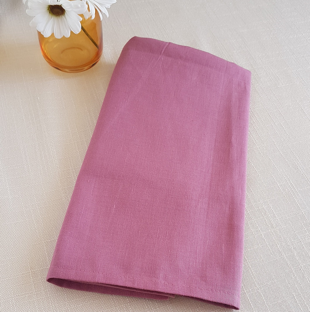 Folded pink fabric on a light beige surface with a small vase of flowers.