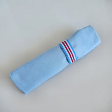 Load image into Gallery viewer, Light blue cotton fabric cutlery wrap holder with red, blue and white striped elastic loop on a light gray background