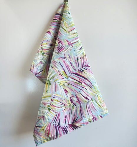 Colourful fabric with abstract palm leaf pattern in green, blues, pinks on a white background