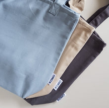 Load image into Gallery viewer, Three handmade cotton bags in different colours- blue, beige, dark grey. Bags have Komo lble on the side.