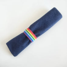 Load image into Gallery viewer, Navy blue linen cutlery wrap with a rainbow elastic loop band on a white background