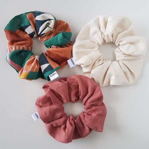 Three scrunchies, two with colorful patterns and one in a solid cream color, all made of cotton and linen, displayed on a white background.